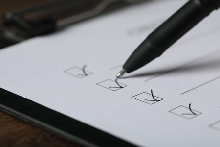 Paper sheet with checkboxes and pen at table, closeup
