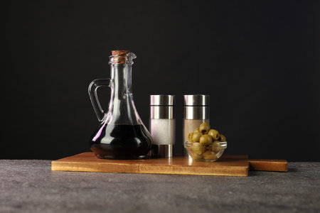 Vinegar in bottle, olives and spices on gray table against black background