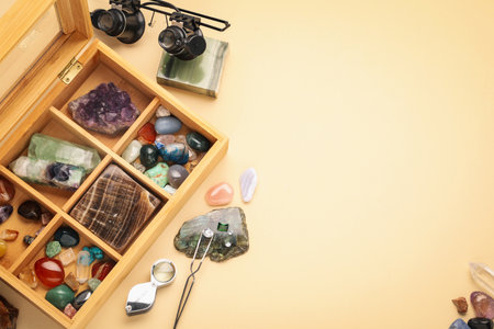 Box with beautiful gemstones and jeweler's tools on beige background, flat lay. Space for textの写真素材
