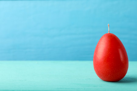 Red egg-shaped candle on turquoise wooden table against light blue background, space for text. Easter decorの写真素材