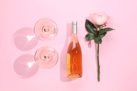 Delicious rose wine in glasses and bottle with flower on pink background, flat layの写真素材