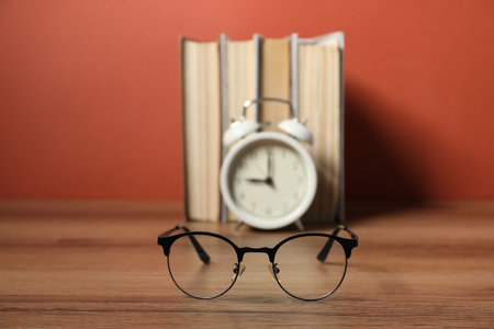 Alarm clock, glasses and books on wooden table, selective focus. Time for knowledgeの写真素材