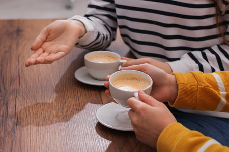 Coffee break. Women with cups of hot drinks at wooden table indoors, closeupの写真素材