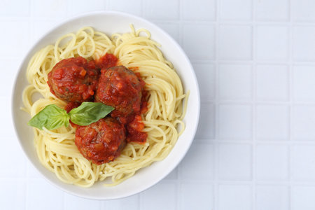 Delicious pasta with meatballs in bowl on white tiled table, top view. Space for textの写真素材
