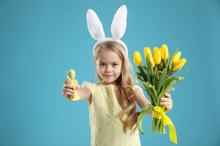 Cute little girl with bunny ears and tulips on light blue background. Easter celebration