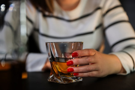 Alcohol addiction. Woman with glass of whiskey at table indoors, closeupの写真素材