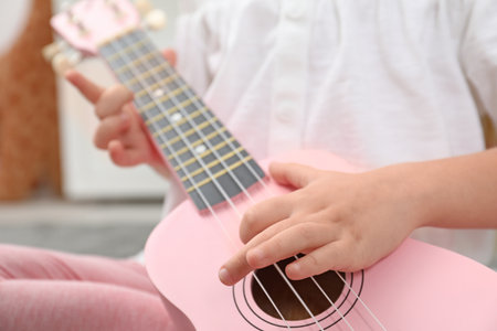 Little girl playing ukulele at home, closeupの写真素材