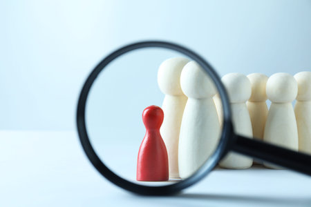 Human resources concept. Looking at wooden figures through magnifying glass on light background,...