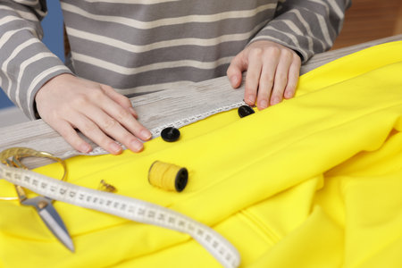Woman measuring jacket with tape and spool of sewing thread at light wooden table, closeupの写真素材