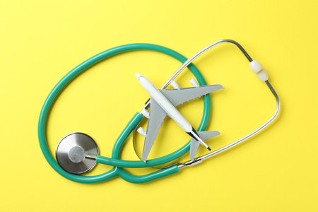 Medical tourism. Stethoscope and plane model on yellow background, flat layの写真素材