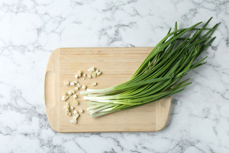 Wooden cutting board and green onions on white marble table, top viewの写真素材