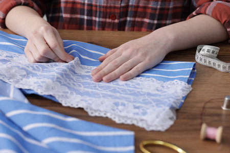 Woman sewing shirt with thread at wooden table, closeupの写真素材