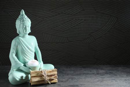 Palo santo sticks and Buddha statue with burning candle on grey textured table against black background, closeup. Space for textの写真素材