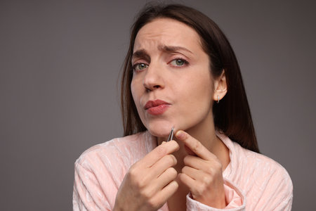 Woman plucking her facial hair with tweeters on gray backgroundの写真素材