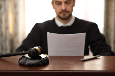 Judge with document at wooden table in office, focus on gavel