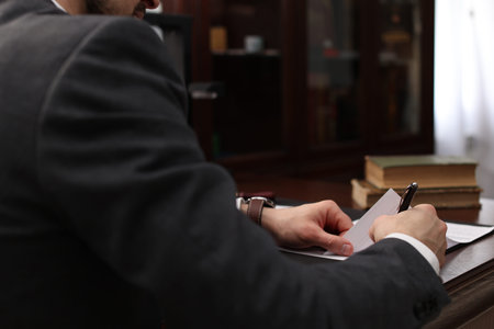 Notary signing document at wooden table in office, closeup