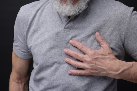 Heart attack. Senior man suffering from pain in chest on black background, closeupの写真素材