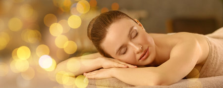 Beautiful young woman relaxing on massage table in spa salon, bokeh effect. Banner designの写真素材