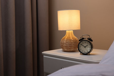 Glowing lamp and alarm clock on nightstand in bedroom. Space for text