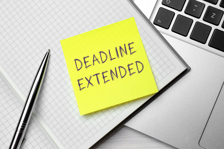 Paper note with text Deadline Extended, notebook, pen and laptop on table, top view