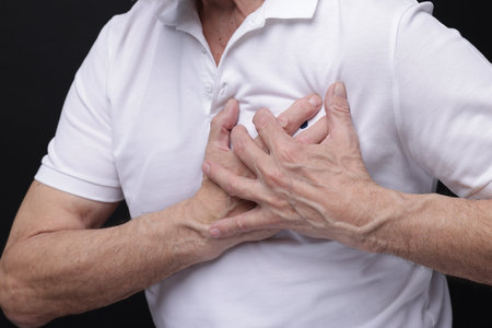 Heart attack. Senior man suffering from pain in chest on black background, closeupの写真素材