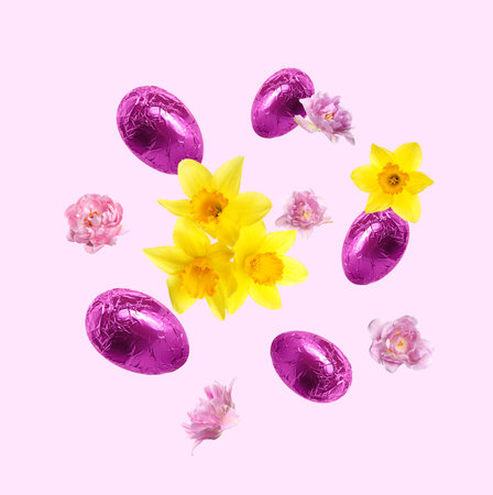 Chocolate eggs wrapped in bright foil and beautiful spring flowers in air on pastel light violet...