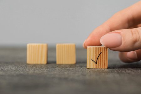 Woman taking wooden cube with check mark at gray table, closeup