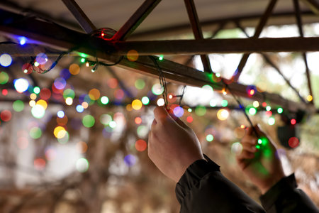 Man decorating house with Christmas lights outdoors, closeup. Space for textの写真素材