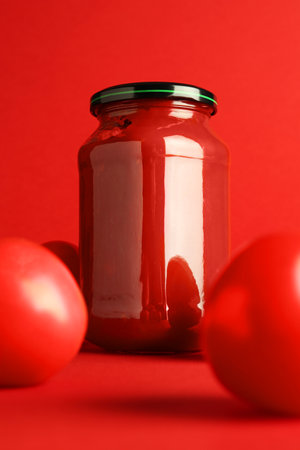 Ketchup in glass jar and fresh tomatoes on red backgroundの写真素材