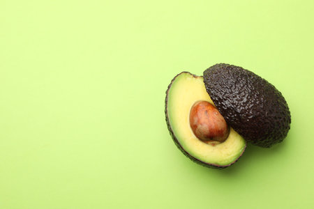 One cut ripe avocado on light green background, top view. Space for text