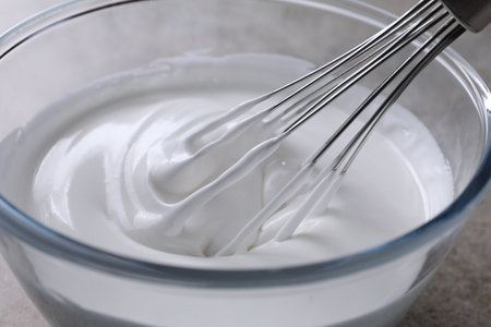 Whisking whipped cream in bowl on gray table, closeupの写真素材