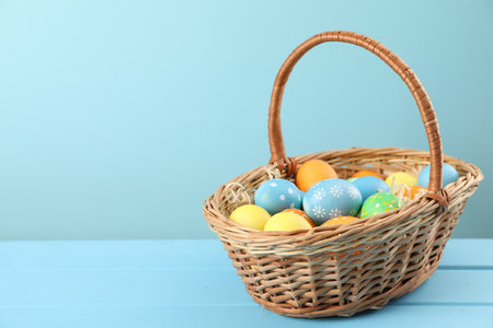 Many decorated Easter eggs in wicker basket on light blue wooden table, space for textの写真素材