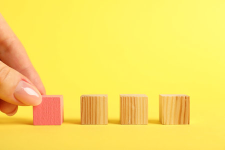 Hand with wooden cubes on yellow background, closeupの写真素材
