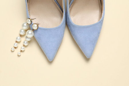 Stylish shoes and pearl earrings on beige background, top view