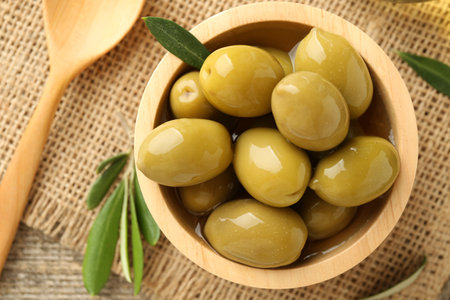 Delicious marinated olives in bowl, green leaves and spoon on table, flat layの写真素材