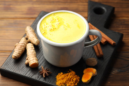 Tasty turmeric latte in cup and spices on wooden table, closeupの写真素材