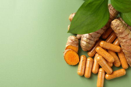 Turmeric rhizomes and capsules on green background, flat lay. Space for text