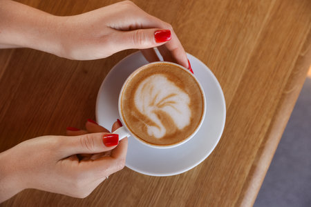 Woman with cup of aromatic coffee at wooden table in cafe, top viewの写真素材