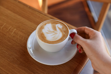 Woman with cup of aromatic coffee at wooden table in cafe, closeup