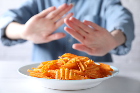 Woman refusing to eat chips at white table, selective focus. Food allergy conceptの写真素材