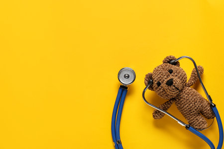 Pediatrics concept. Toy bear with stethoscope on yellow background, top view. Space for textの写真素材