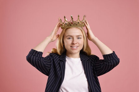 Smiling businesswoman in elegant crown on dusty pink backgroundの写真素材