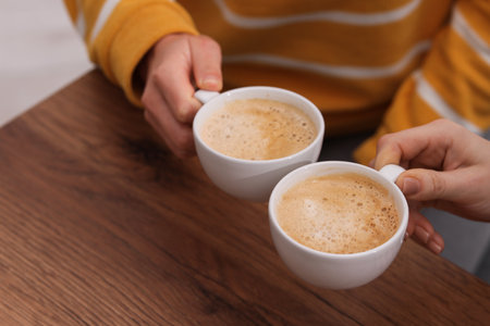 Coffee break. Women with cups of hot drinks at wooden table indoors, closeupの写真素材