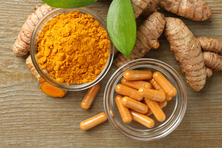 Turmeric capsules, powder, roots and green leaves on wooden table, flat layの写真素材