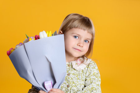 Cute little girl with bouquet of tulips on orange backgroundの写真素材