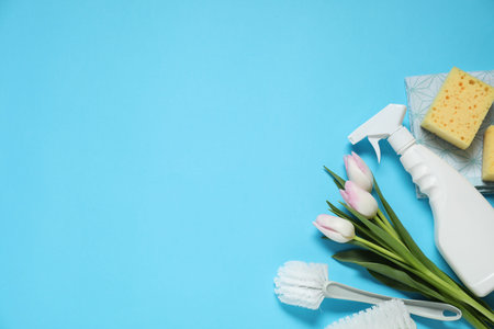 Spring cleaning. Detergent, supplies and tulips on light blue background, flat lay. Space for text