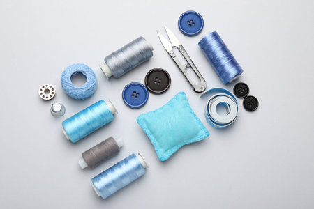 Different sewing supplies on light grey background, flat lay