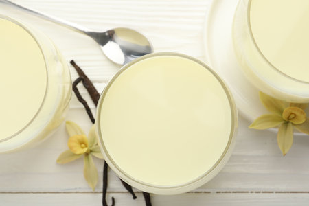 Delicious vanilla milk in glasses, pods and flowers on white wooden table, flat layの写真素材