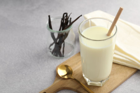 Delicious vanilla milk in glass, pods and spoon on grey table, space for textの写真素材
