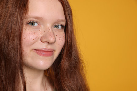 Beautiful teenage girl with freckles on orange background, closeup. Space for textの写真素材